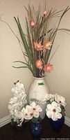 Full view of the four faux floral arrangements showing the large white vase and three smaller vases with white and peach flowers.