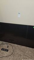 Photo of front lower section of the television showing part of screen and black bezel with remote and cords on the carpet.