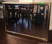 Front view of gold framed rectangular wall mirror reflecting table and chairs.