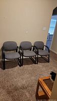 Three gray fabric office chairs with black metal cantilever frames arranged side by side.