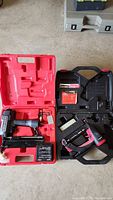 Four pneumatic nailers and staplers in their respective carrying cases placed on the ground showing general overview of contents.