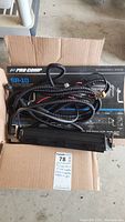 Light bar kit in an open cardboard box on a concrete floor, showing the bundled wiring harness and part of the light bar.