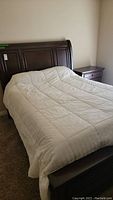 Overview of dark wood queen sleigh bed with white comforter, showing headboard and footboard