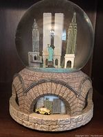 New York City snow globe with stone-arched base and miniature landmark figures and yellow taxi