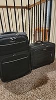 Two black Samsonite suitcases on carpet near stair railing, one larger and one smaller