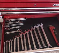 Top drawer showing a range of combination wrenches and one small red pipe wrench on a black drawer liner.