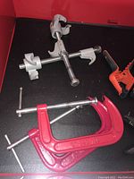 Metal clamps including a 6" red C-clamp and silver pipe clamps in a red storage bin.