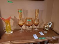 Full view of the art glass vase, two amber glass vases, pedestal bowl, and two stemware glasses on a wooden surface.