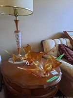 Photo showing two amber-colored art glass sculptures on a wooden table next to a lamp and couch.