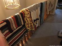 Multiple blankets and hand-sewn quilts draped over stair banister showing a variety of colors and patterns.