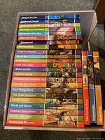 Box containing 24 colorful hardback Childcraft children's books arranged spine up showing titles related to educational and storytelling content.