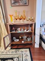 Wood cabinet with open metal screen doors showing some contents inside and various glass and ceramic decorative items on top.
