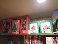 Photo of multiple boxed Christmas decorations on a shelf including a talking tree, an animated bear, and two Traditions Santa Shelf Sitters.