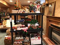 Full view of shelves holding multiple Christmas decorations including figures, greenery, tins, and lighted house
