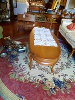 Oval wood coffee table on floral carpet, with carved curved legs, polished surface, with lace runner on top.