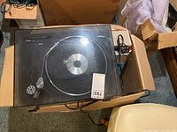 Top view of the LXI series semi-automatic turntable with clear plastic cover showing dust and scratches, tone arm and platter visible