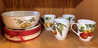 Photo showing Royal Worcester Evesham serving bowl, Dora Papis coffee cups, and Easy Life Fruit Garden plates inside a wooden cabinet shelf.