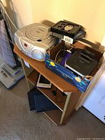 Shelf with several electronic items including a Sylvania portable CD player stereo, Apple iPod, Philips radio, and a key finder in a box.