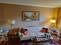 Pair of matching table lamps set on wood side tables in a living room with a beige tufted sofa and framed landscape painting in background.