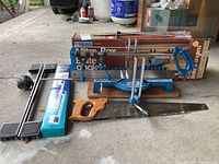 Mitre box with original box, wooden hand saw, appliance rollers, drawing compass on floor.