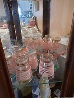 Six small pink glasses with clear rims and criss-cross diamond pattern inside a display cabinet.