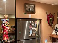 View of framed whiskey-themed wall art above refrigerator, red decorative shield on wall, and refrigerator with assorted magnets