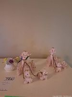 Full view of vintage pink ceramic poodle figurine set with 1 large and 3 small poodles chained, alongside two Radnor floral porcelain figurines.