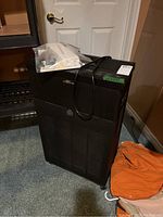 Full view of black rectangular RespirAide air purifier unit with plastic bag of manual and extra parts on top.