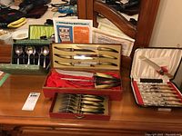 Photo showing multiple cutlery sets including a boxed Empire Sheffield stainless steel set with opal horn handles, and two other boxed sets with knives, forks, and spoons.