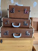 Front view of three stacked vintage Langmuir Airway suitcases showing white handles, metal locks and brown textured surfaces