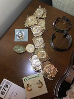 Photo of assorted goldplate belt with coin motifs, two cuff bracelets, and small earrings on cards.