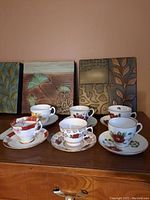 Photo showing six vintage teacups with matching saucers placed on wooden surface in front of decorative wall panels