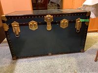 Closed view of black McBrine steamer trunk with brass hardware and metal rivets on corners and edges.