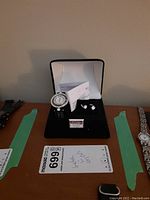 Photo of the Elizabeth Taylor women's watch and matching stud earrings set displayed in an open black jewelry box with papers inside.
