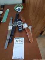 Photo showing five watches lined up on a wooden surface, visible brand names and varied strap styles.