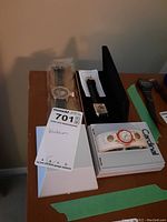 Three watches shown including a Cardinal watch in original packaging, a gold-tone metal link band watch, and a square face watch with dark strap.