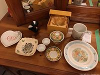 Top view of entire lot showing all items including Wedgwood Peter Rabbit plate and cup, Asian dishes, Carrigcraft plate, heart-shaped plate and figurine.