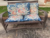 Front view of resin wicker loveseat with floral cushions showing overall condition and seating area.