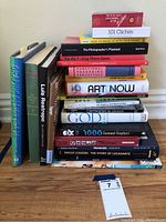 Photo displaying the full collection of stacked hardbound books on art and fashion with a variety of titles and colorful covers.