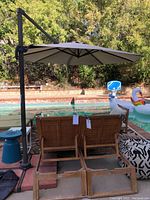 Side view of cantilever patio umbrella with beige fabric canopy open, wooden chairs and other patio items nearby.