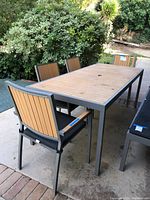 Full view of the rectangular metal frame patio dining table with four matching chairs on concrete patio, showing wood slat table top and chair backs.