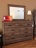 Front view of dresser with seven drawers and matching mirror on top, showing handles and wood grain texture.
