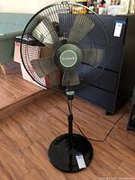 Full view of the Holmes oscillating floor fan on wooden floor near a couch and cabinet.