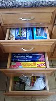 Kitchen drawers opened showing various boxes of plastic wrap, aluminum foil, parchment paper, and plastic bags.
