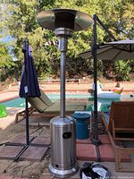 Full view of stainless steel propane patio heater by pool with base, tall middle pole, and wide top reflector.