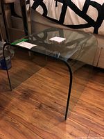 Curved clear glass end table showing one side and top, placed on wood floor near couch.