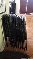 Stack of eleven black metal folding chairs viewed from the side showing folded positions and legs