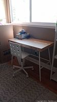 Desk with wooden top and white metal legs shown against a wall under window, with chair in front.