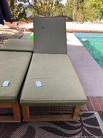 Wooden lounge chair with green cushions placed beside a pool. Cushions have tags and appear lightly used.