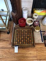 Overview of lacquered wood chess board with intricate South Asian style border and several partially used candles in various sizes and colors grouped around it.